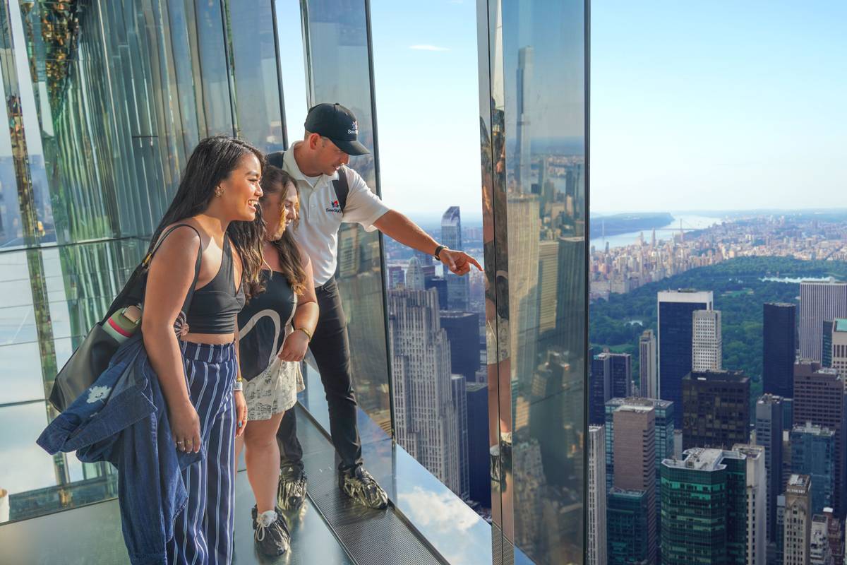 Tour guide with visitors at Summit One Vanderbilt overlooking NYC skyline.