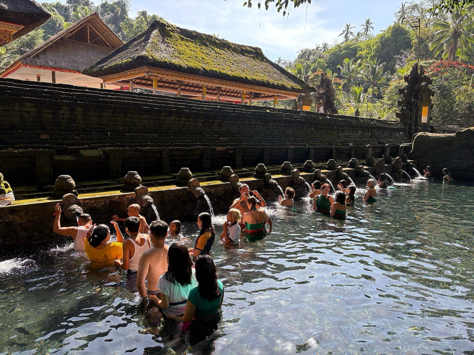 Bathers in sarongs stand in the clear spring-fed pool at Pura Tirta Empul, waiting their turn under the stone water spouts