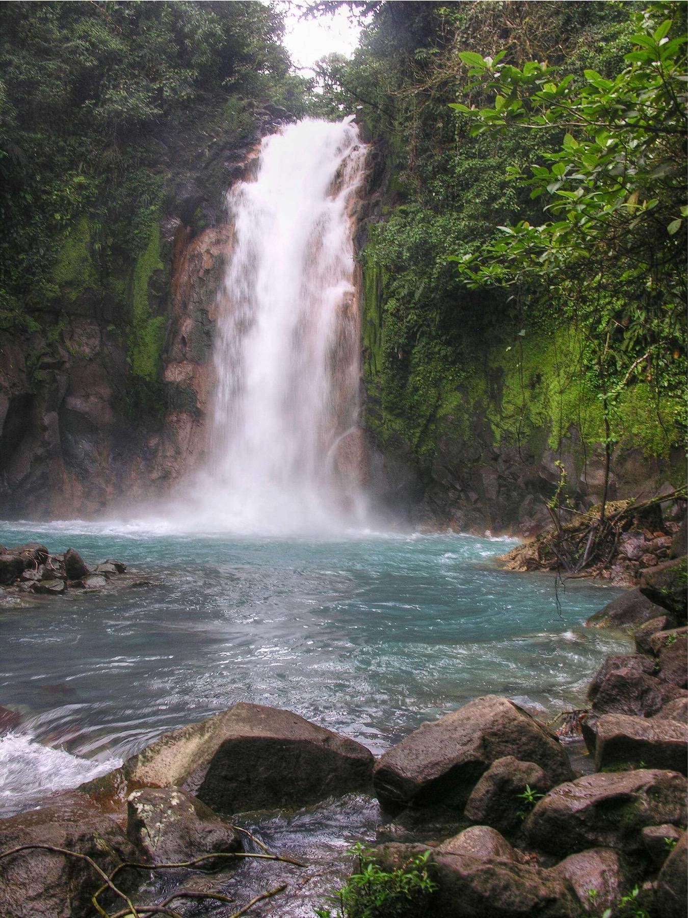 The Río Celeste waterfall dropping into a turquoise pool framed by mossy rock and rainforest
