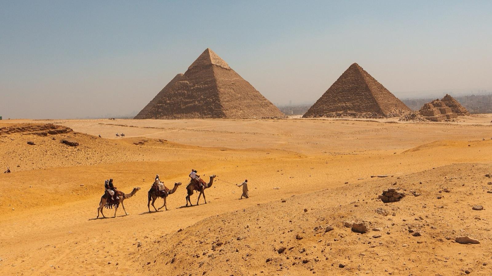 A camel caravan crosses the sand in front of the pyramids of Khafre and Khufu at Giza