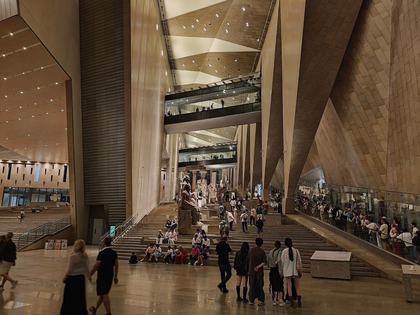 Visitors on the grand staircase of the Grand Egyptian Museum, lined with ancient statues