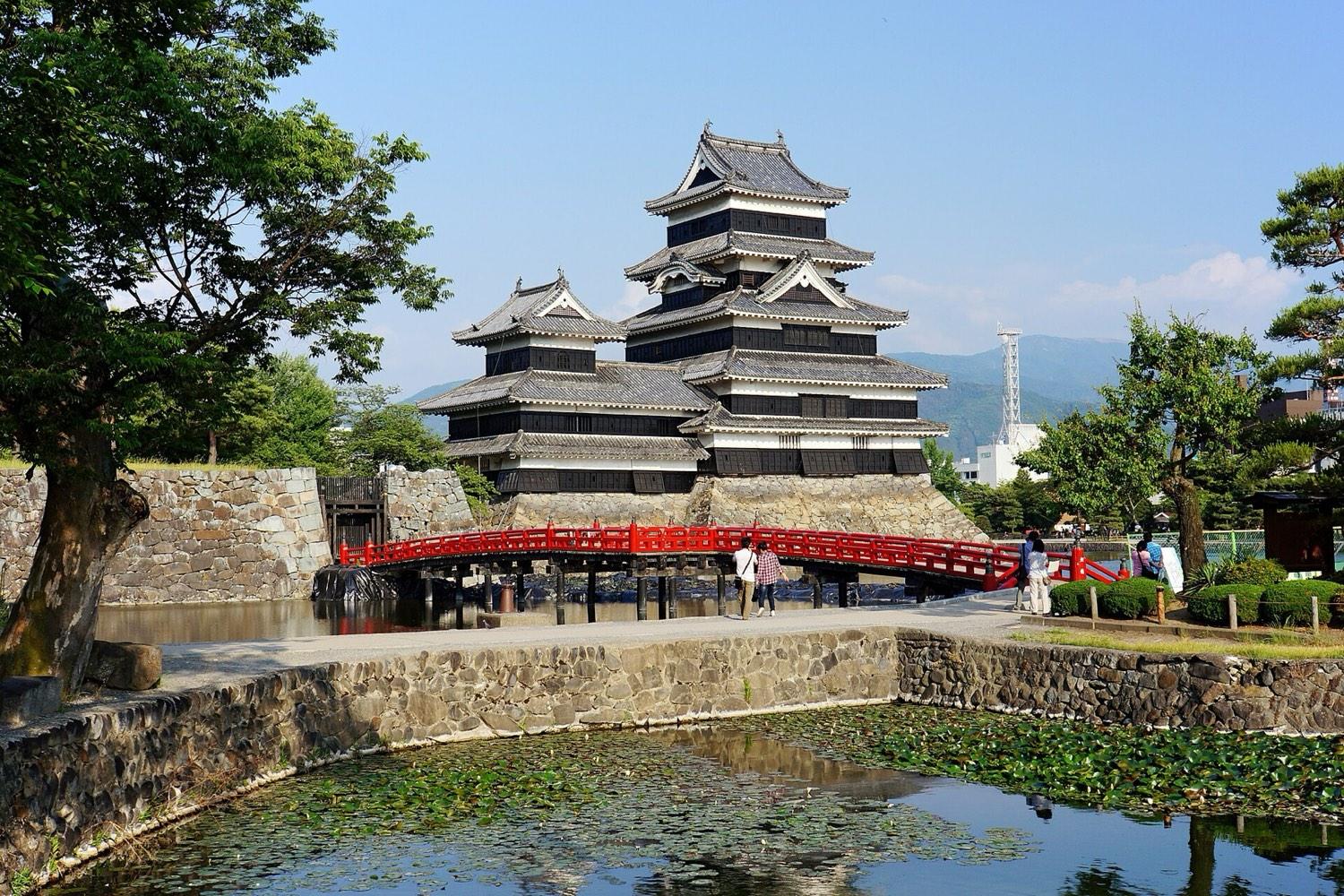 The black and white keep of Matsumoto Castle reflected in its moat, with the red Uzumi bridge