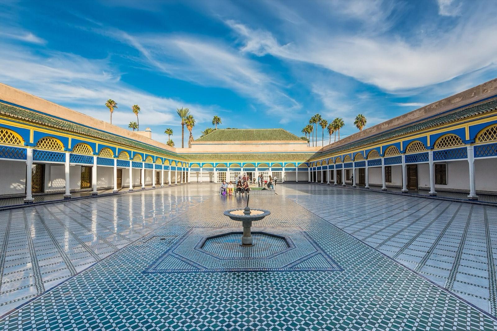 The large marble courtyard of the Bahia Palace in Marrakech, with blue and yellow arcades and a central fountain