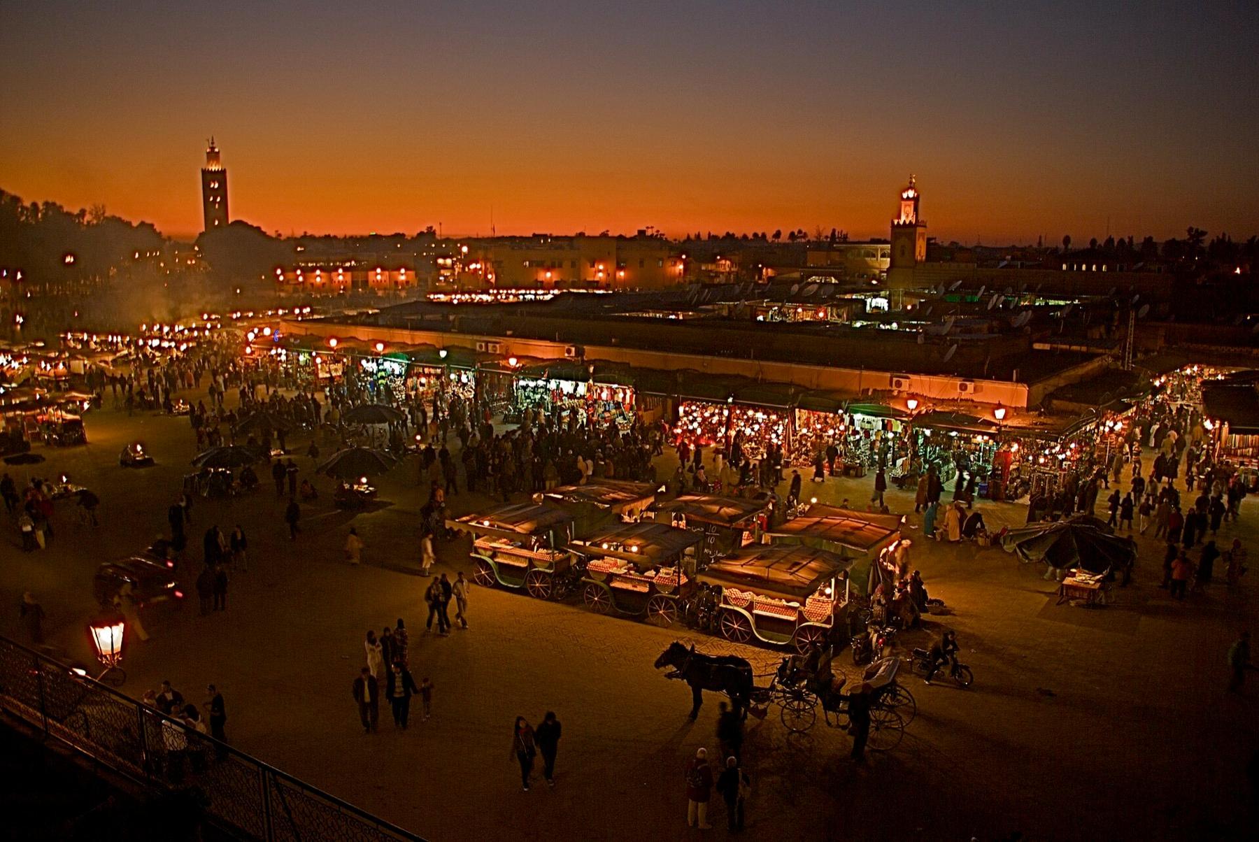 Djemaa el-Fna at dusk, its food stalls lit up below an orange sky and the Koutoubia minaret