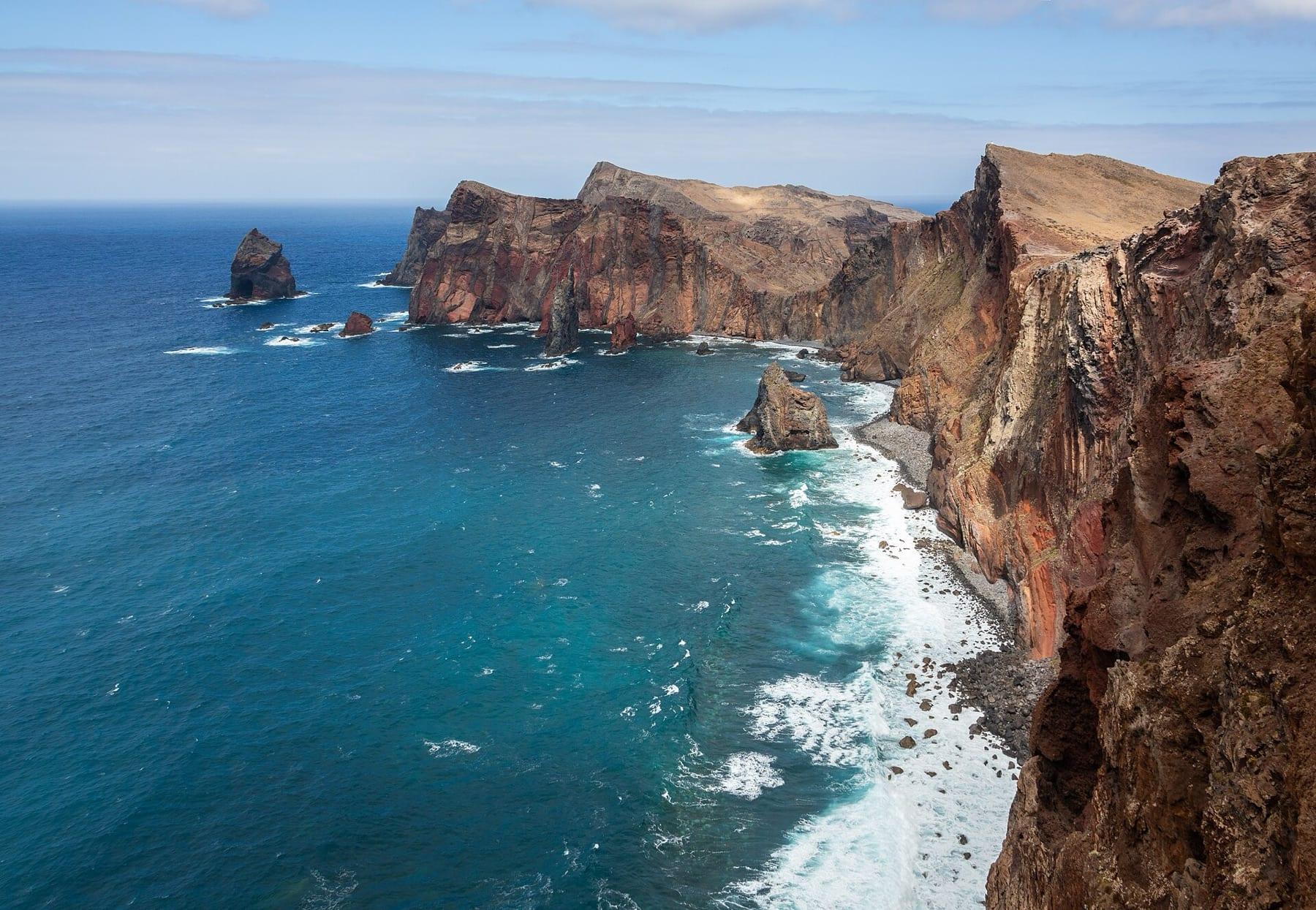 Red and ochre sea cliffs and rock stacks on the Ponta de São Lourenço peninsula above a turquoise Atlantic