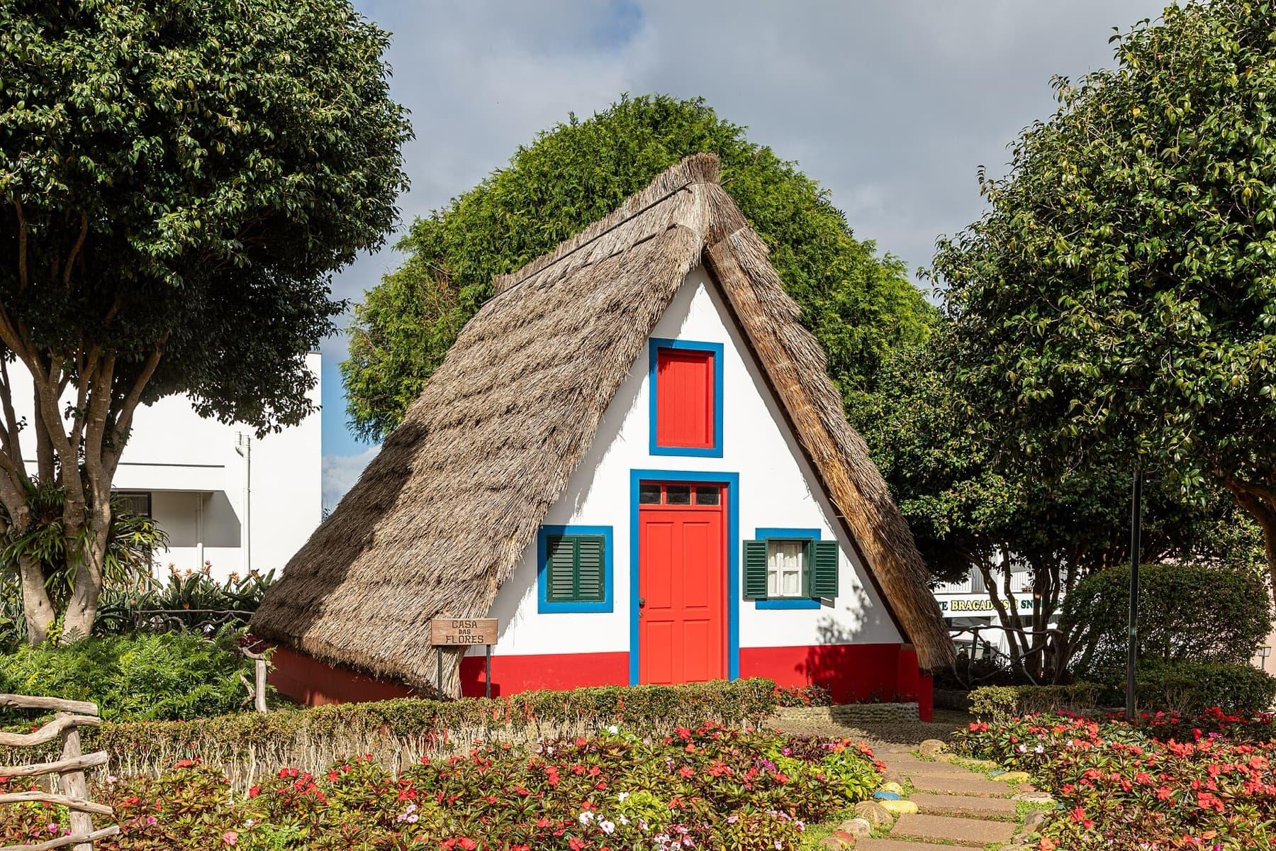 A traditional triangular thatched house in Santana, painted white with a red door and blue window frames