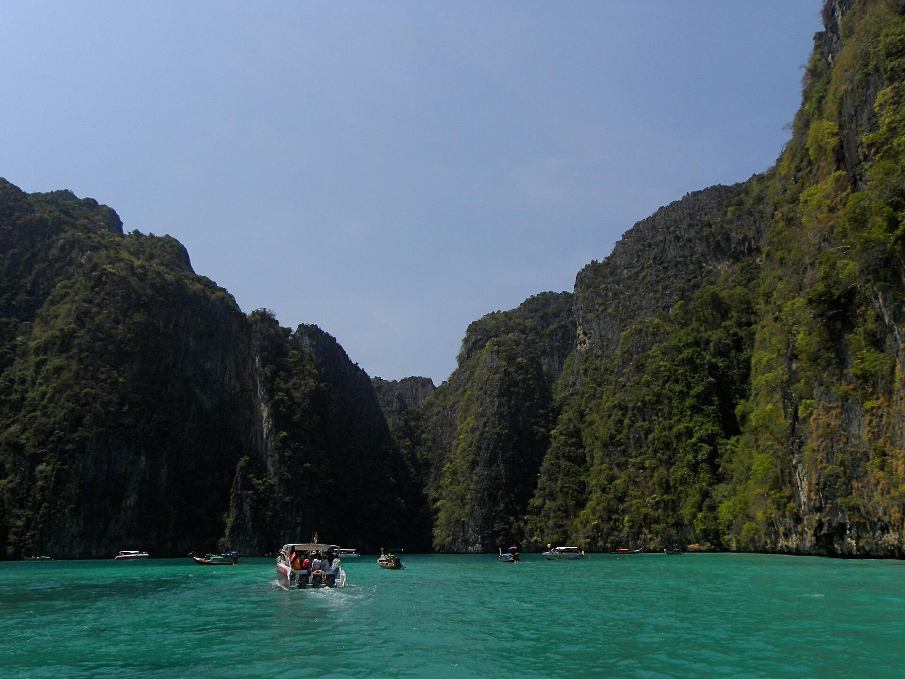 Green water between tall jungle-covered cliffs in Pileh Lagoon, with a speedboat entering