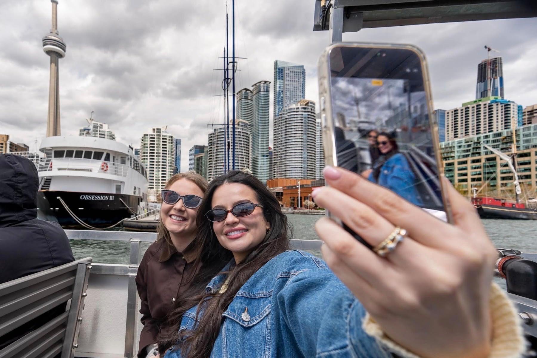 Three guests take a selfie at Toronto's Harbourfront with the CN Tower and the downtown skyline behind them