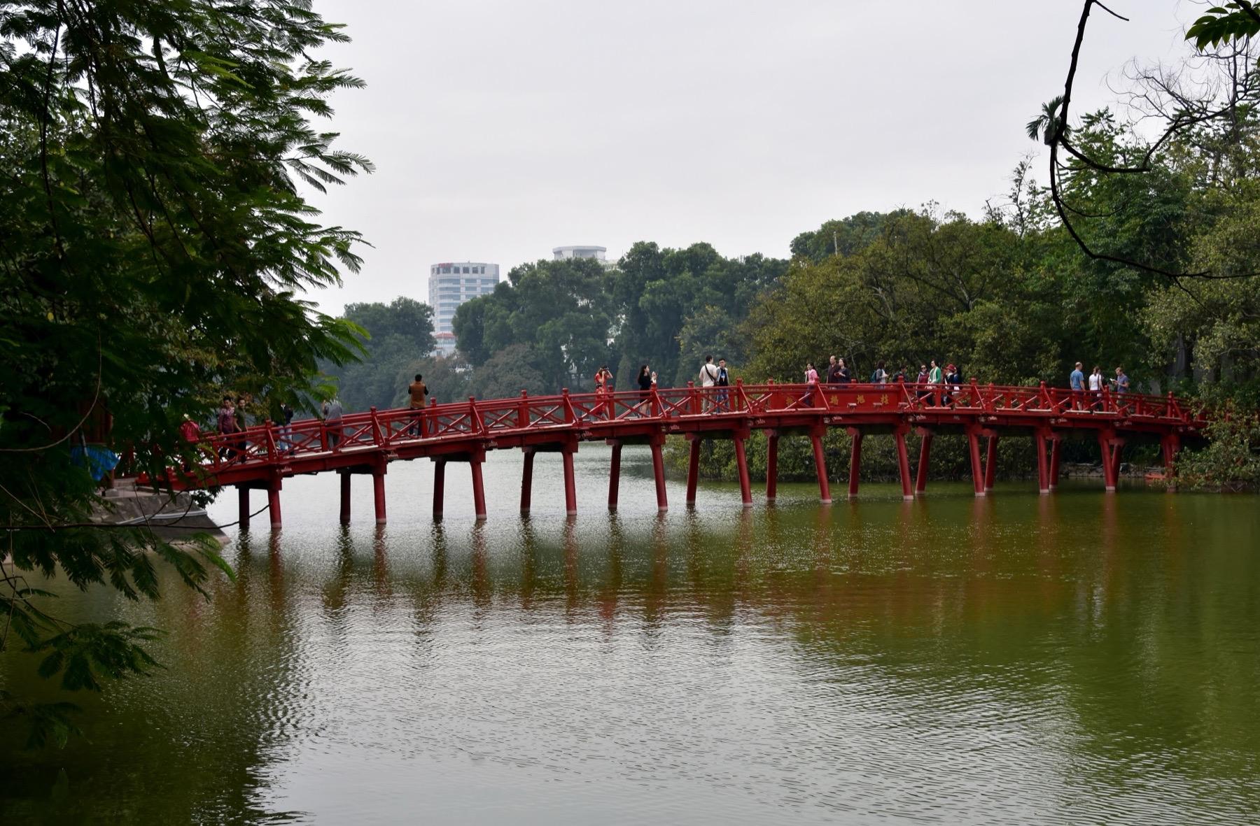 The red wooden The Huc Bridge crossing Hoan Kiem Lake in Hanoi, with people walking over it