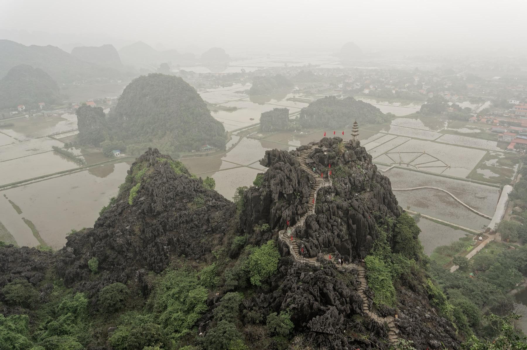View from the Mua Cave viewpoint over a stone stairway on a limestone ridge, flooded rice fields and karst hills near Tam Coc