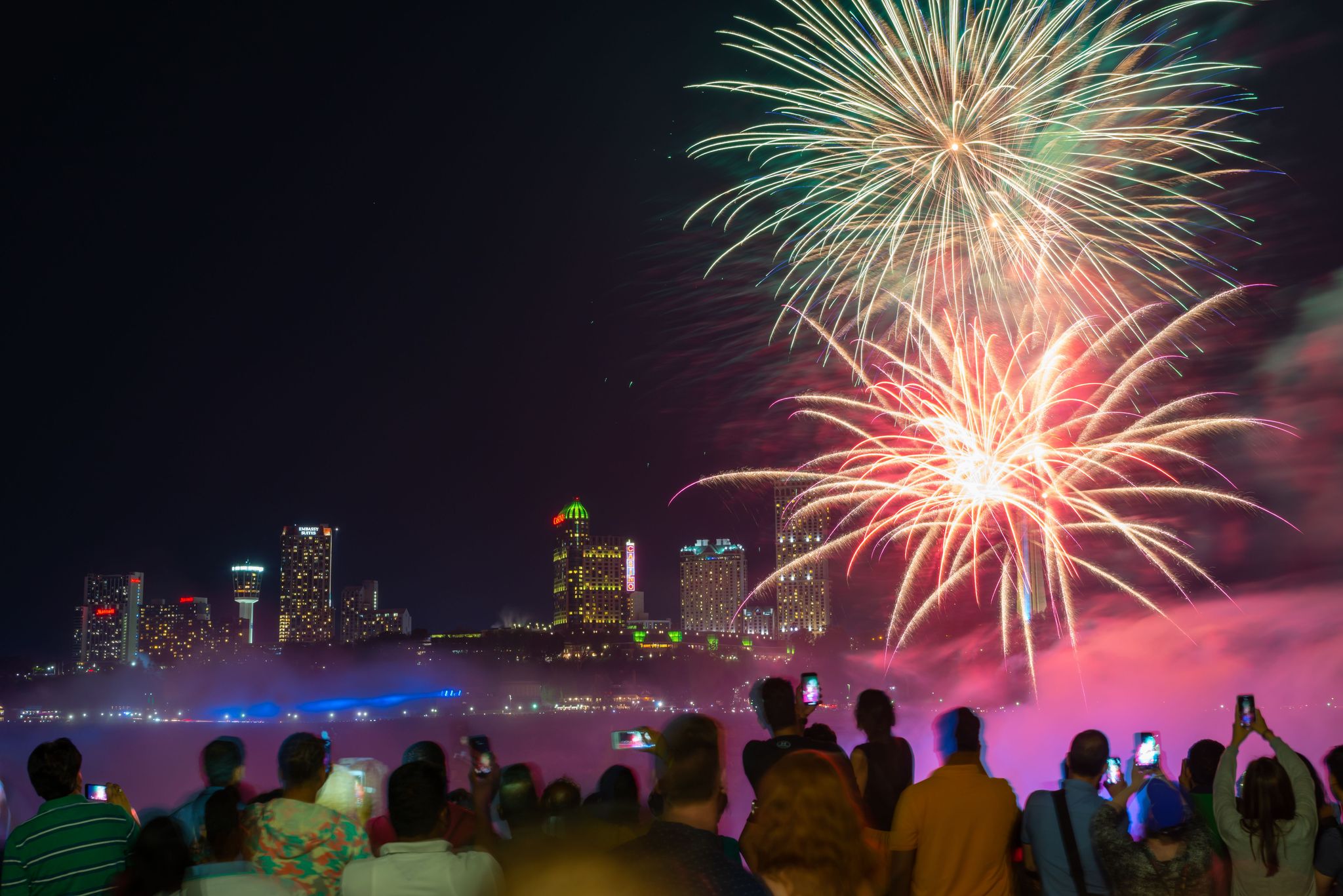 Visitors capturing fireworks over Niagara Falls at night.
