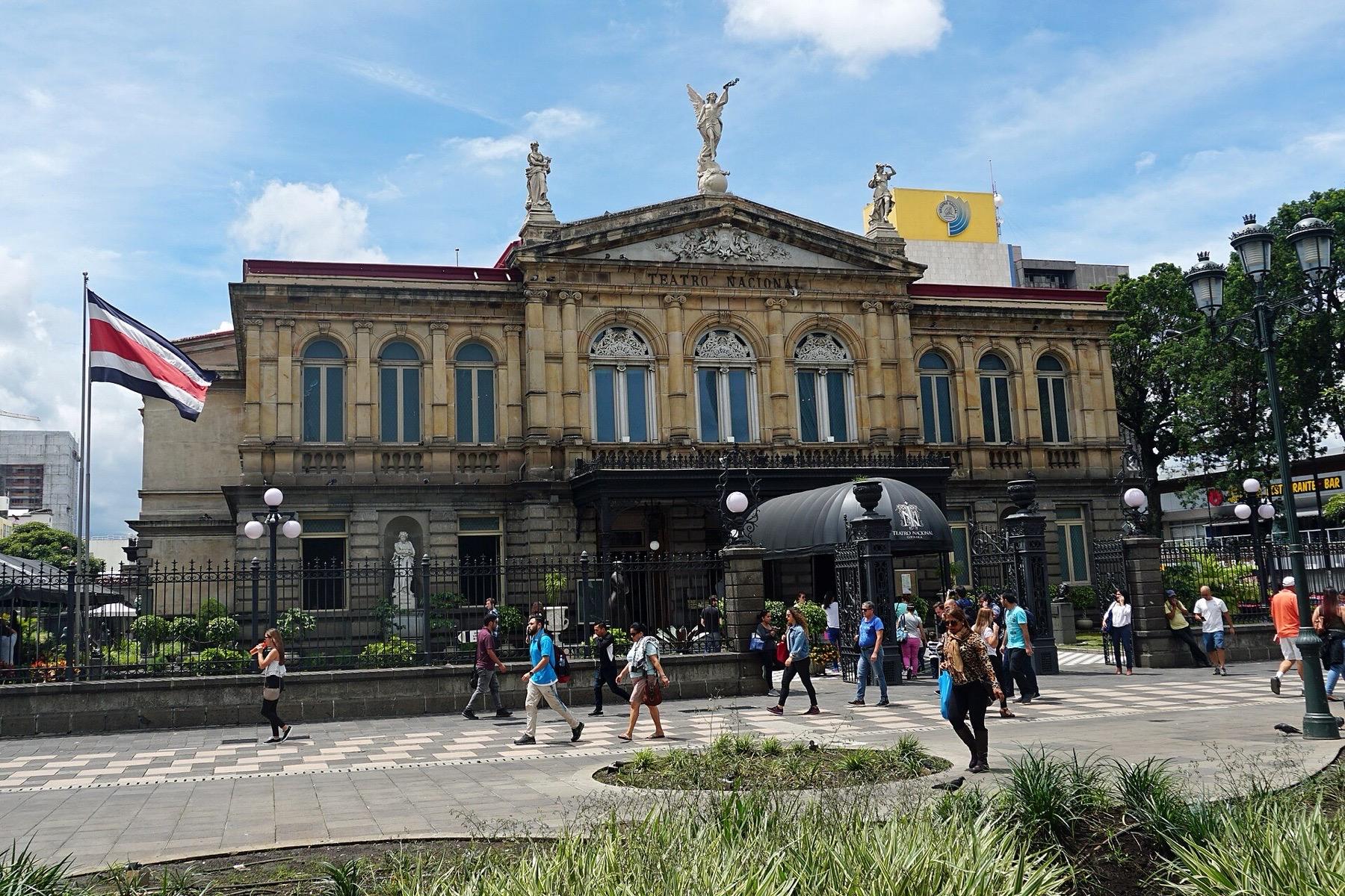 The sandstone facade of the Teatro Nacional in San José, with statues on the roofline and people crossing the plaza