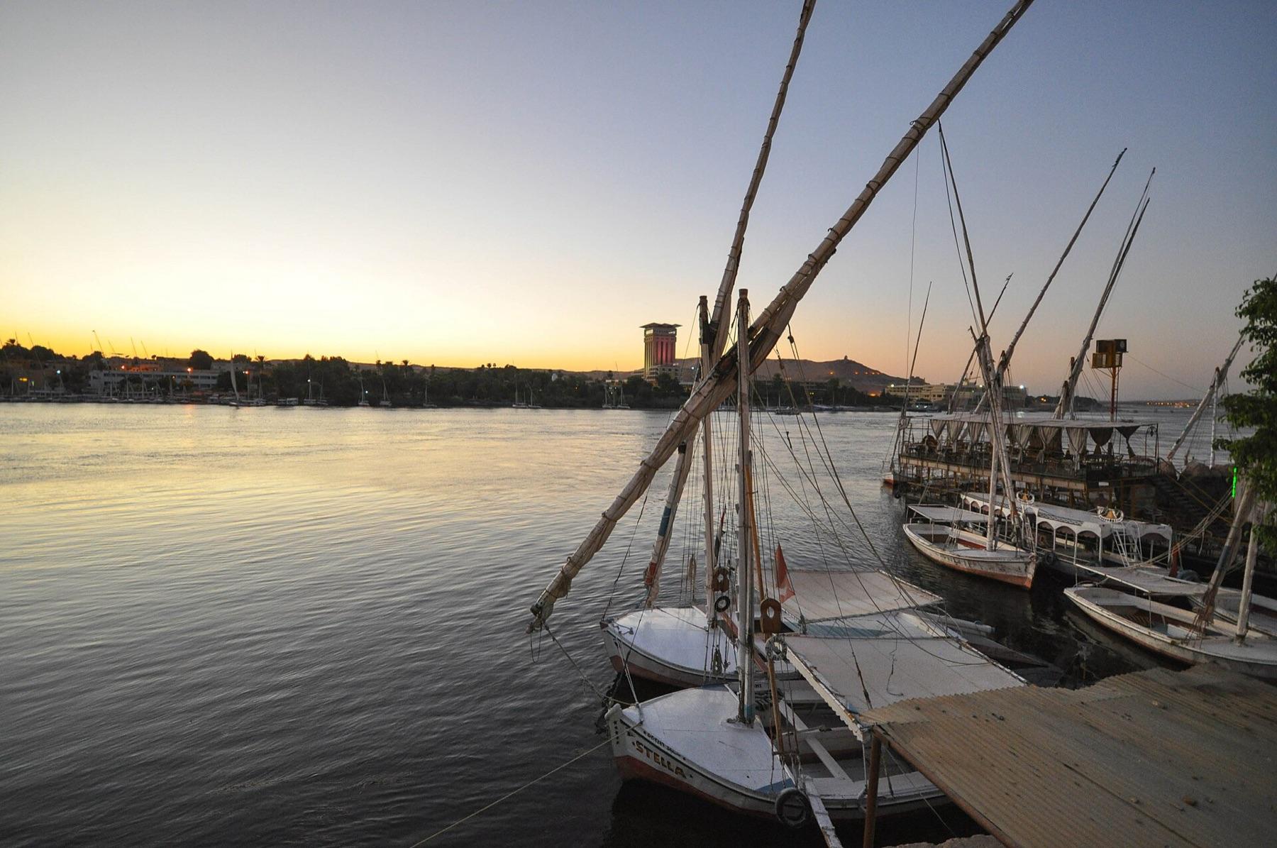 Feluccas moored on the Nile at Aswan as the sun sets over the west bank
