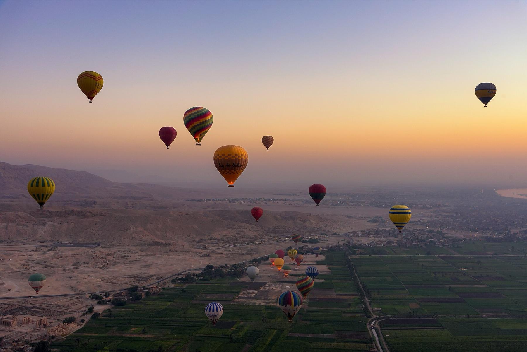 Hot air balloons drift at sunrise over the Theban hills and the green fields of Luxor's West Bank