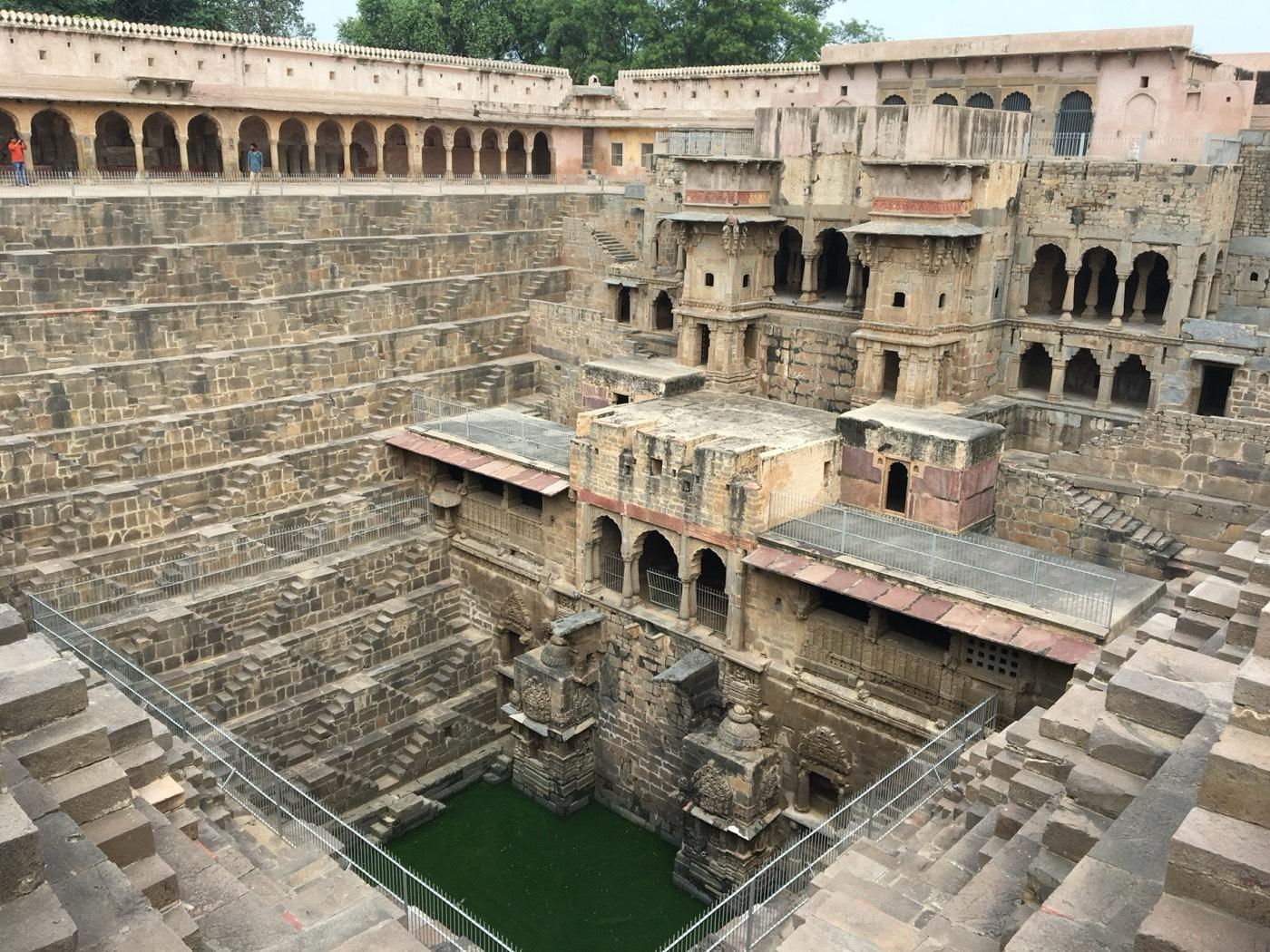 Zigzag flights of stone steps descend on three sides to green water at the bottom of the Chand Baori stepwell