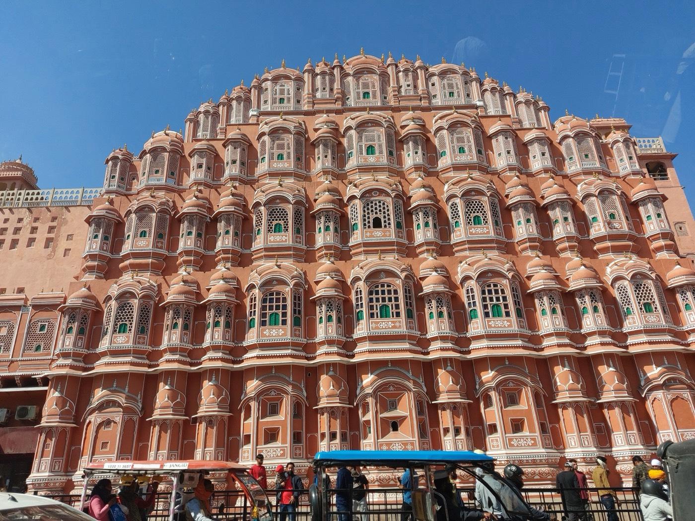 The pink sandstone front of the Hawa Mahal in Jaipur, rows of small windows rising five storeys under a blue sky