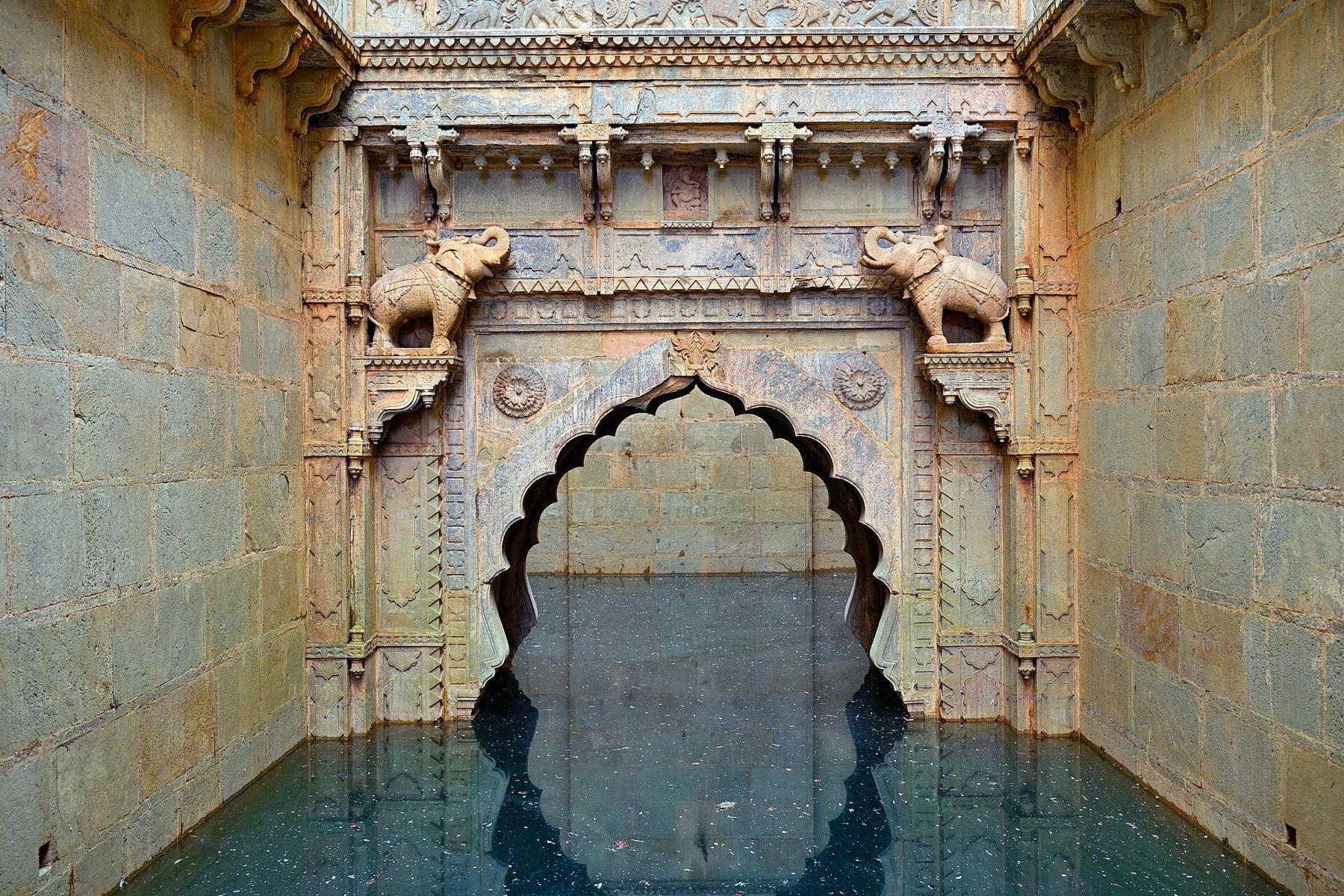 Carved stone elephants and a scalloped arch above the water at the bottom of Raniji ki Baori stepwell in Bundi