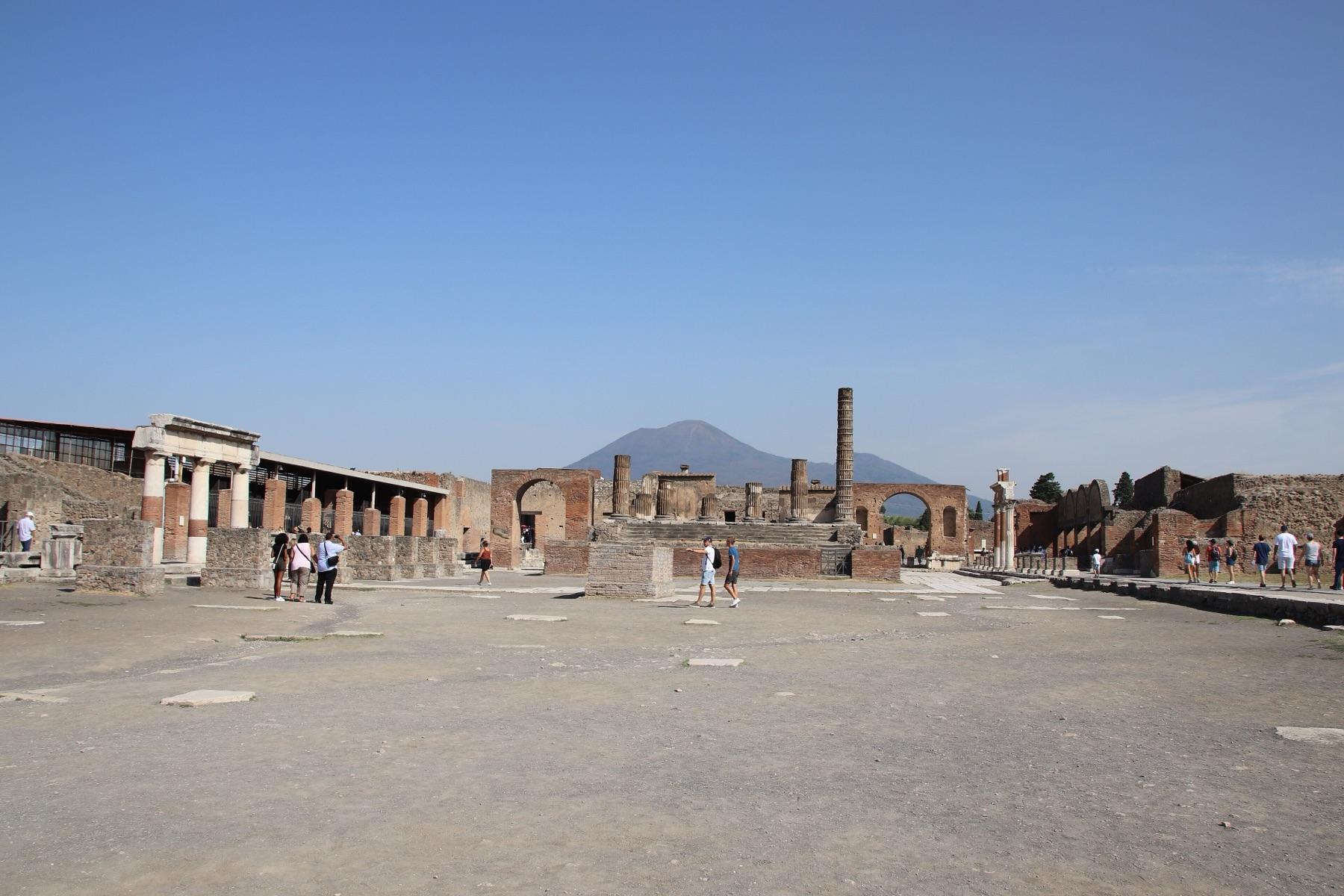 The Forum of Pompeii, a wide open square with ruined columns and arches and the cone of Vesuvius behind