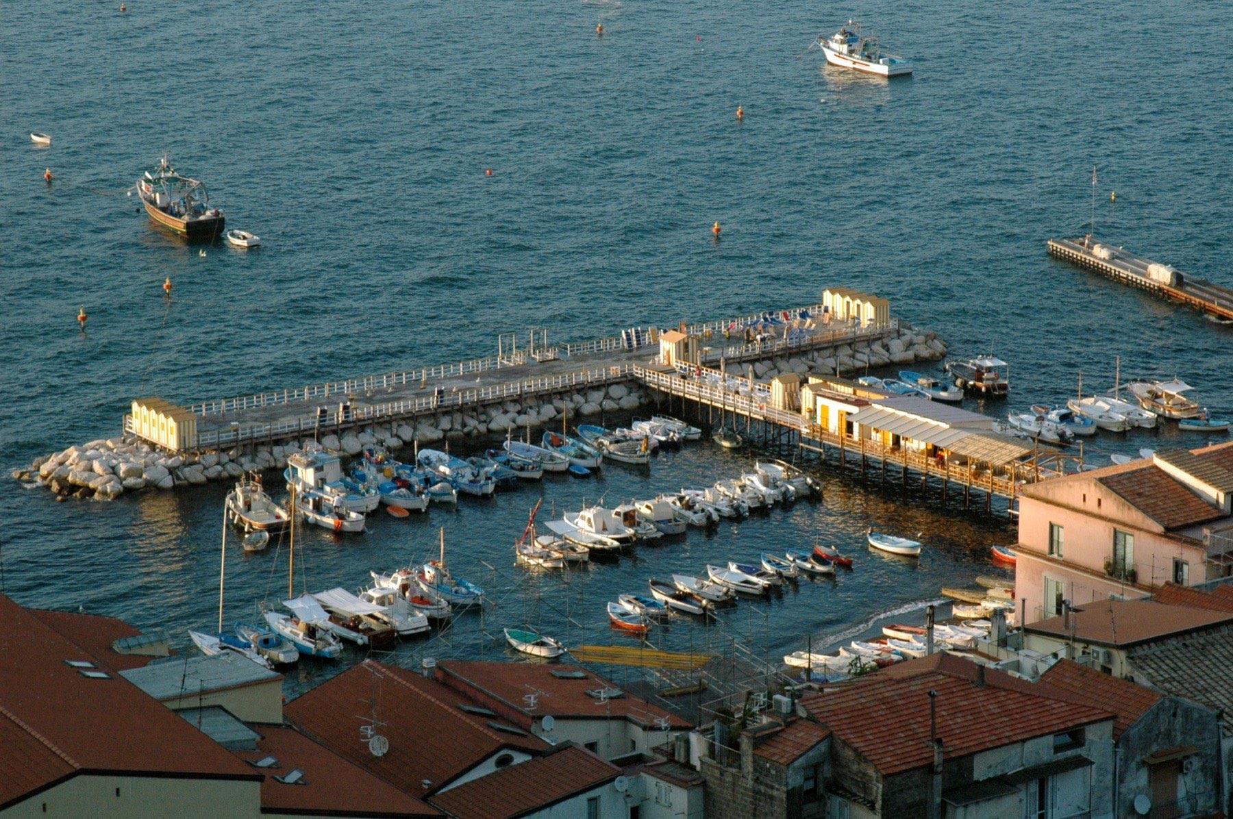 Fishing boats moored in the small harbour of Marina Grande in Sorrento, seen from above at golden hour with red roofs in the foreground