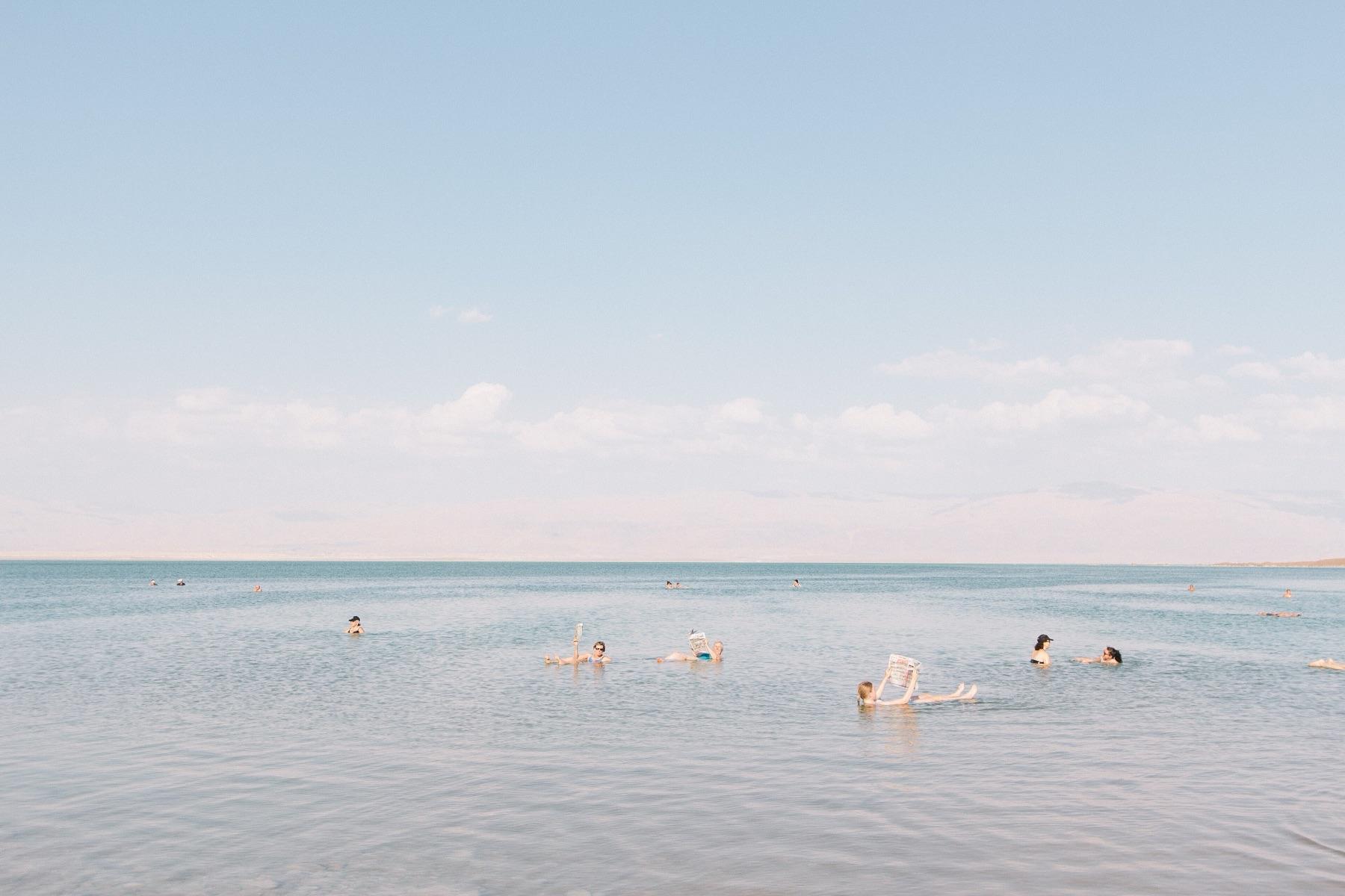 Swimmers float on their backs in the still, pale water of the Dead Sea