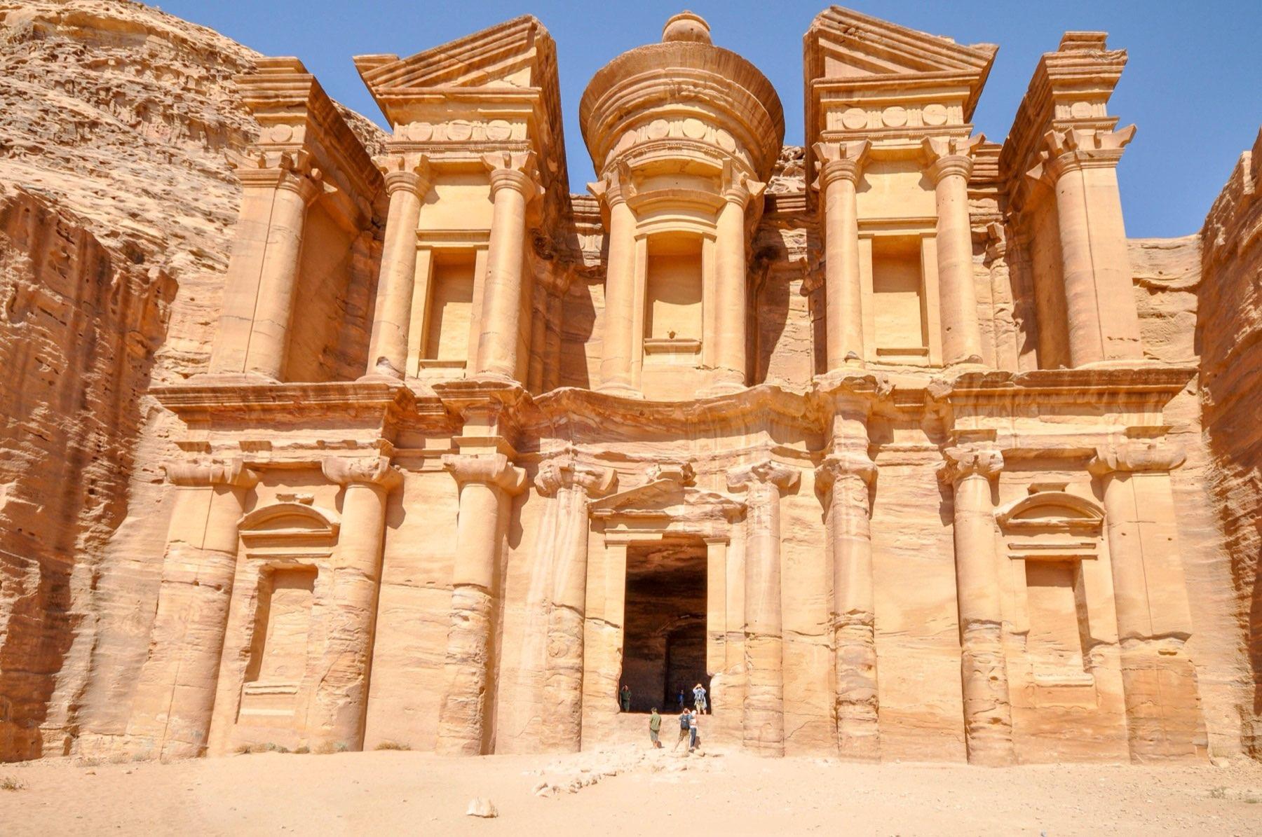 The Monastery at Petra, a huge columned facade carved into a cliff, with small figures of visitors in front