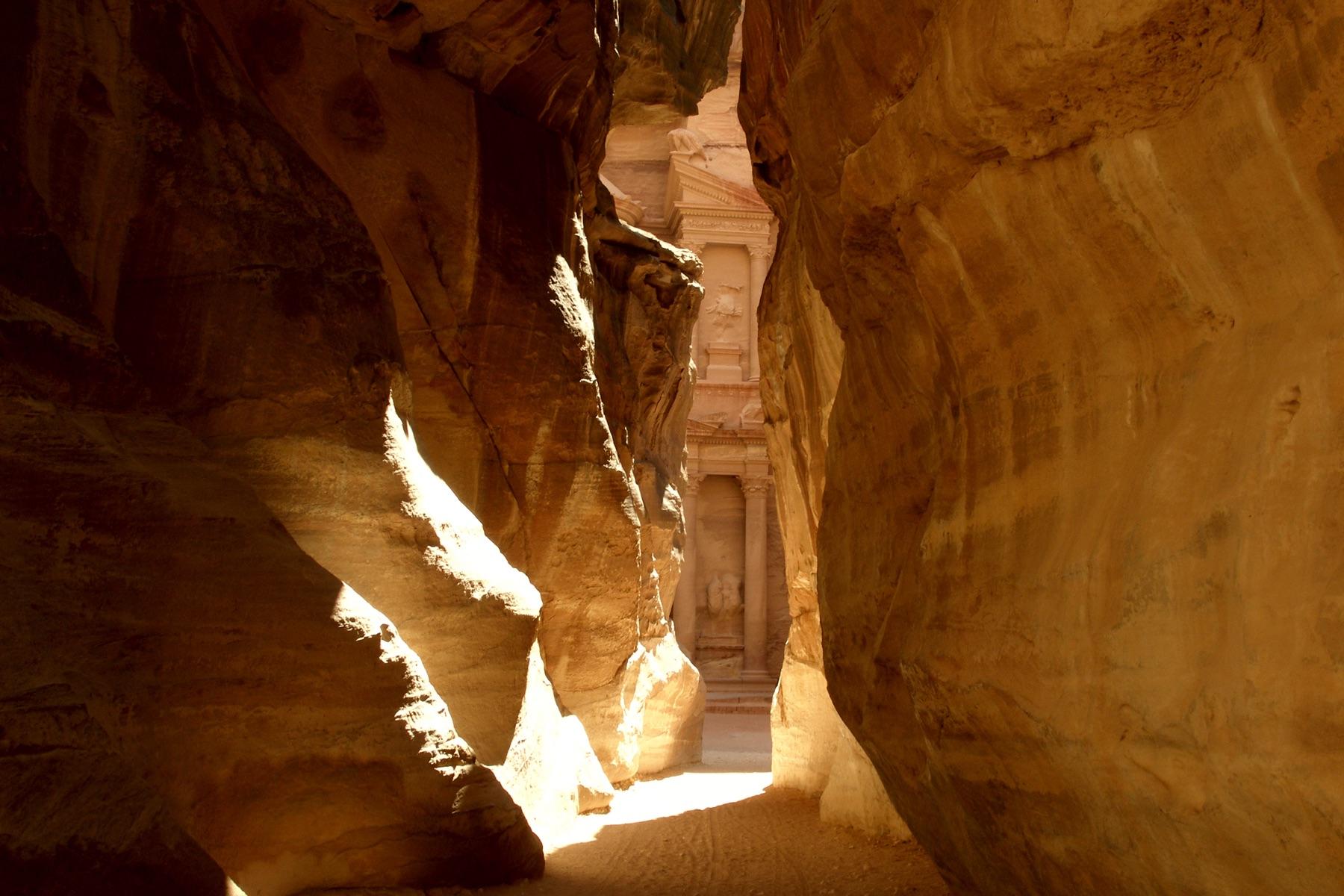 Sunlit sandstone walls of the Siq narrow towards a first glimpse of the Treasury facade