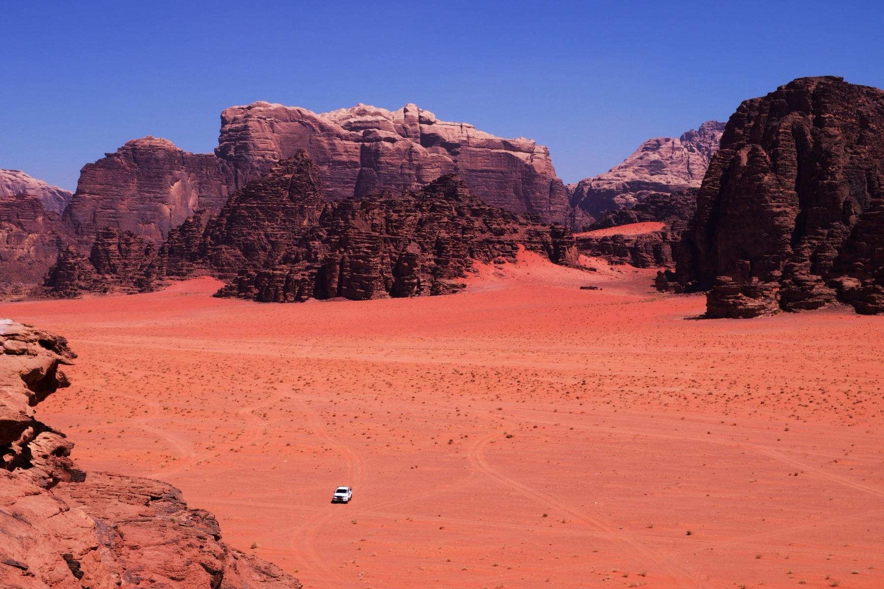A 4x4 crosses red sand between sandstone mountains in Wadi Rum