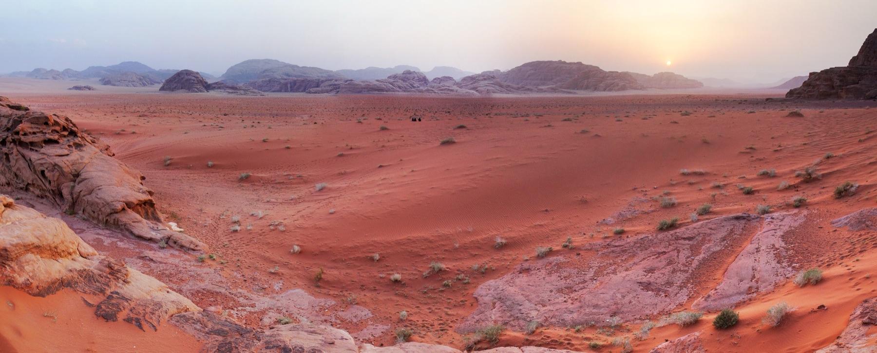 The sun sets low over a wide desert plain and distant ridges in Wadi Rum