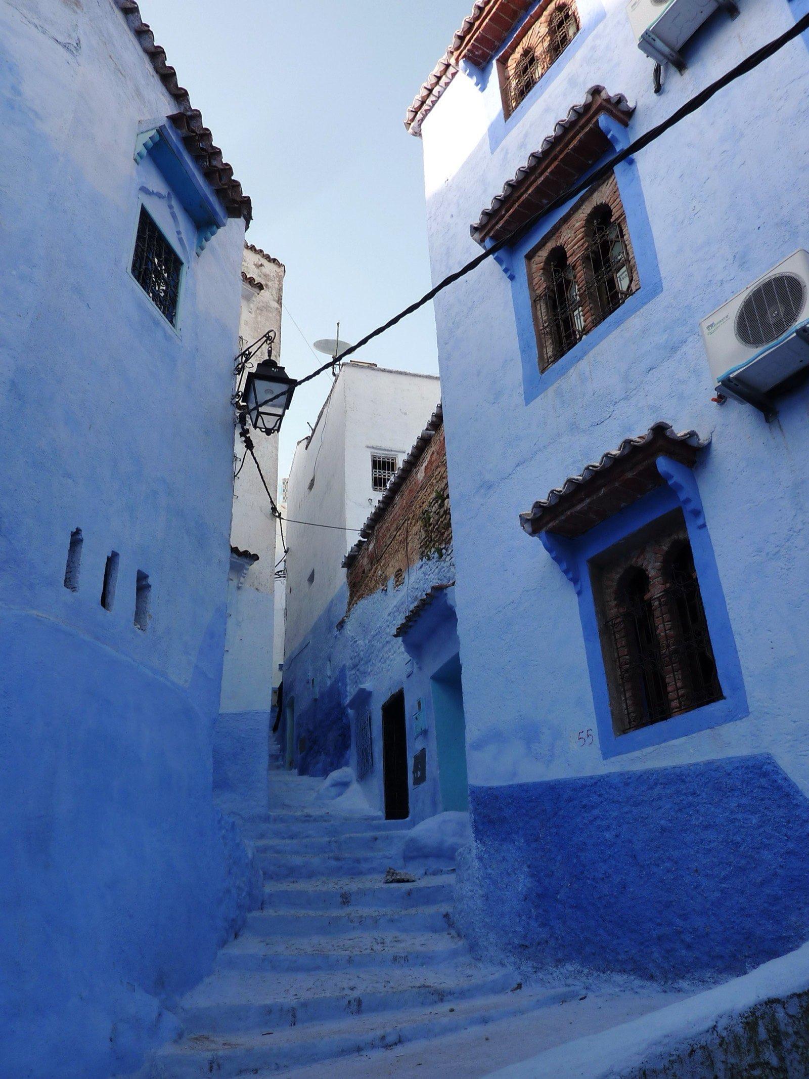 A stepped lane between blue-washed houses with tiled window hoods in the Chefchaouen medina