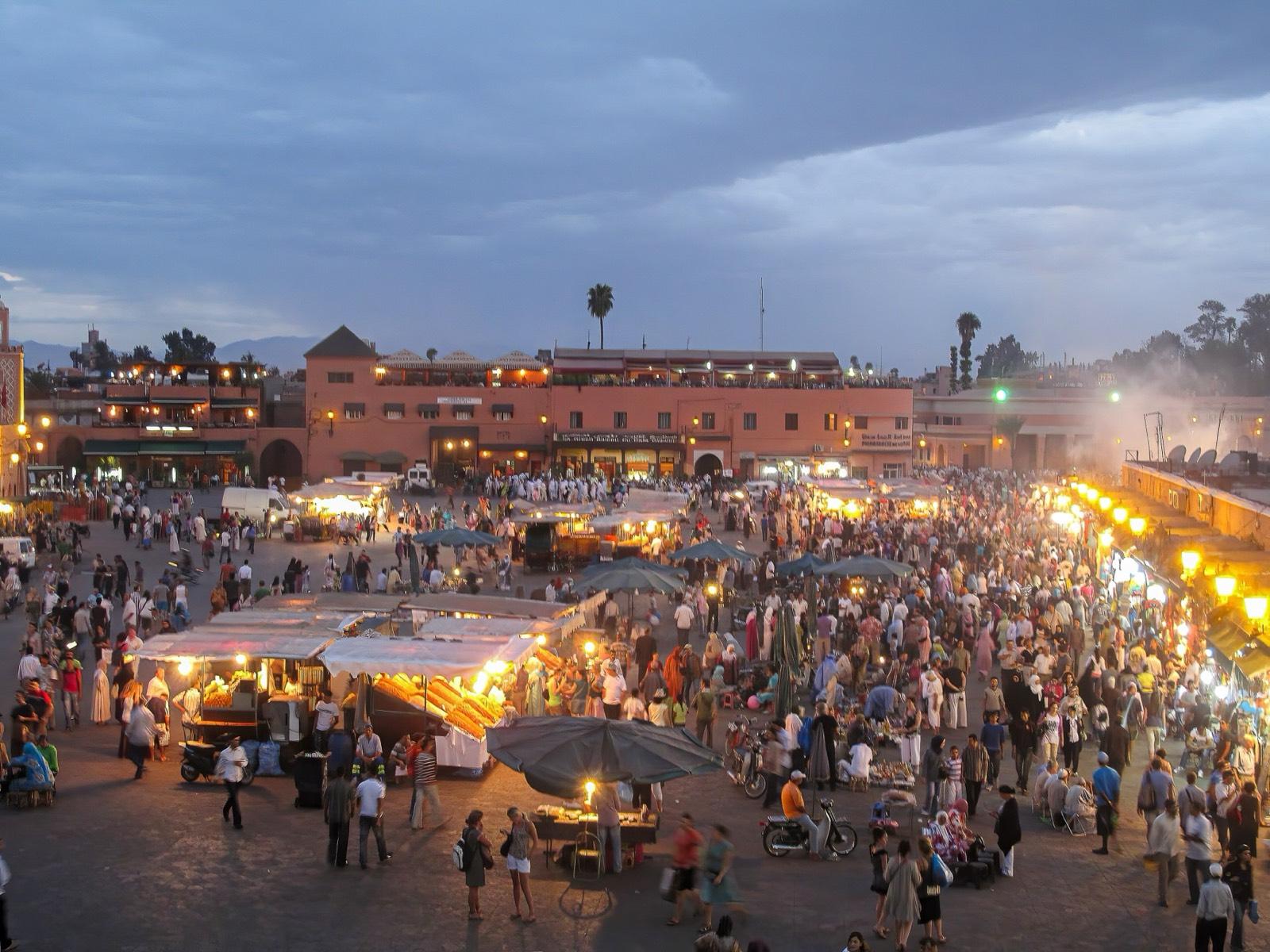 Jemaa el-Fna square in Marrakech at dusk, with lit food stalls, smoke and crowds