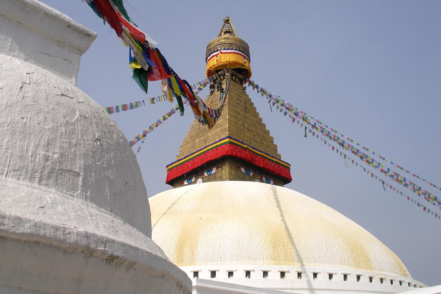 The gilded spire and painted eyes of Boudhanath stupa in Kathmandu, strung with prayer flags