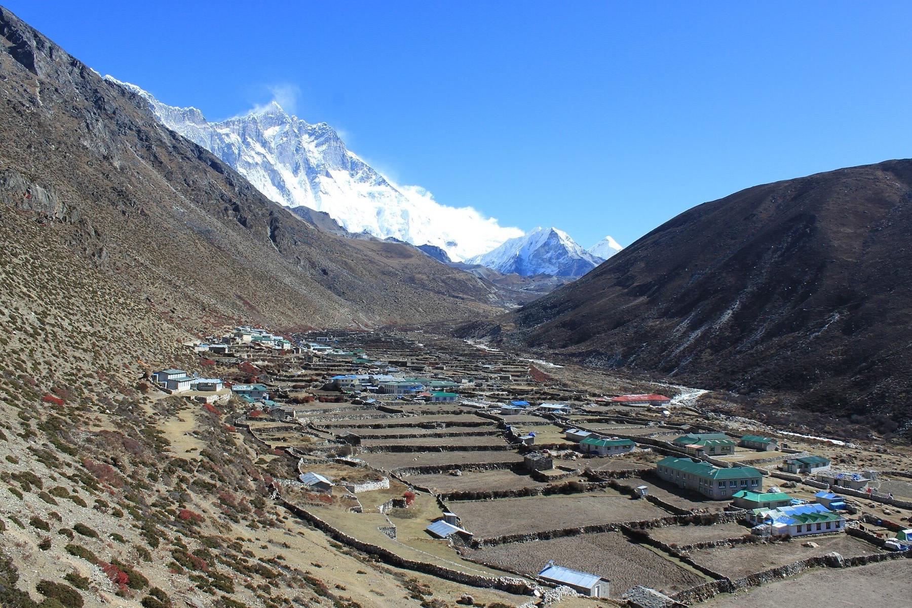 Stone-walled fields and lodges of Dingboche in a wide valley, with the snow face of Lhotse at the head of the valley