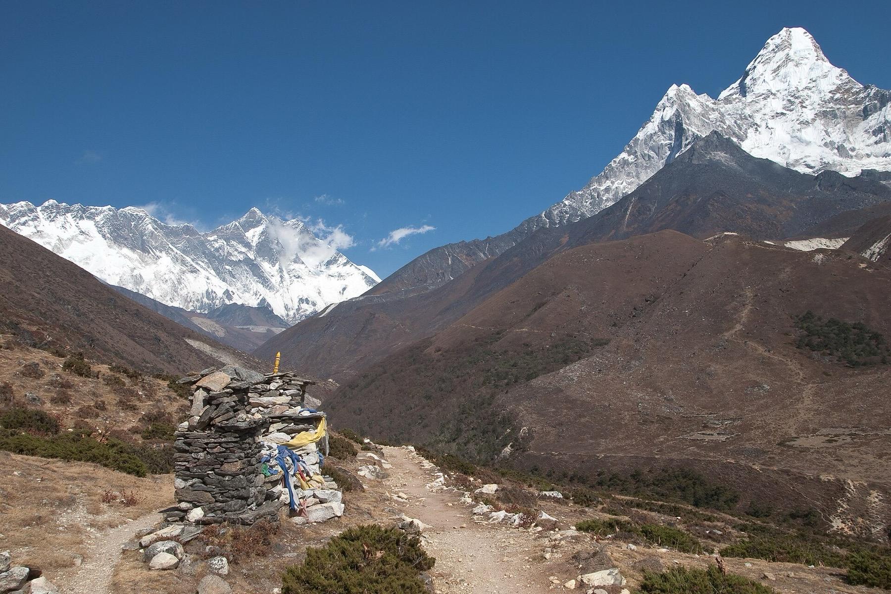 A stone chorten with prayer flags beside the trail near Pangboche, with Ama Dablam rising on the right and the Everest and Lhotse ridge on the left