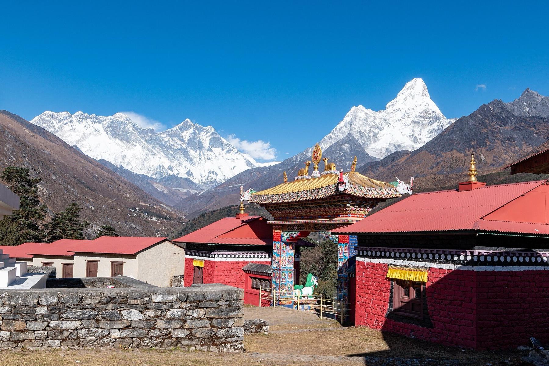 The red and gold gate of Tengboche Monastery with Everest, Lhotse and the sharp peak of Ama Dablam behind under a clear sky