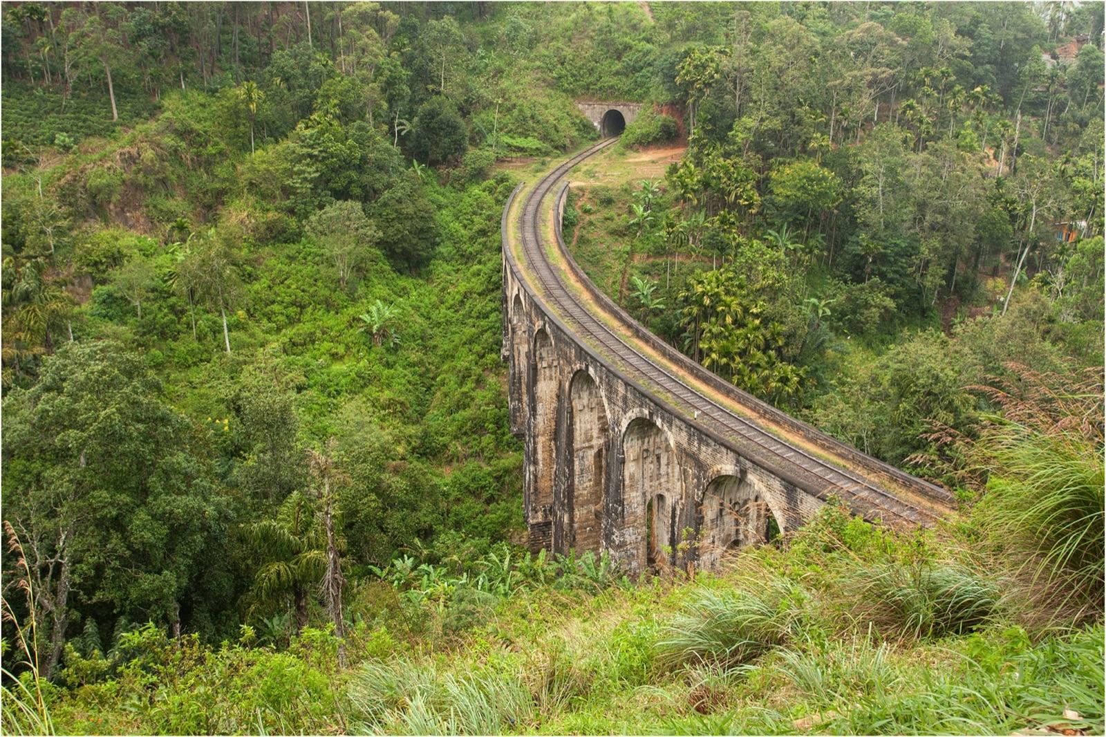 The curved stone Nine Arch Bridge near Ella crossing a green valley towards a railway tunnel