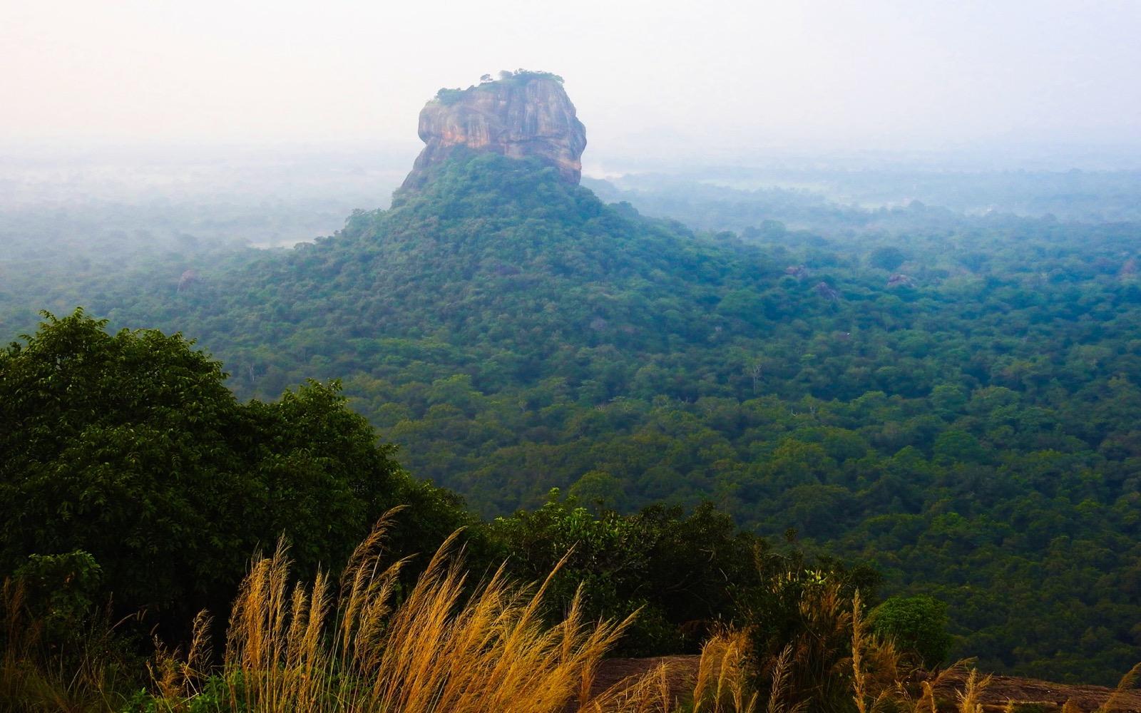 Sigiriya Rock seen from the top of Pidurangala Rock in soft morning haze over the forest