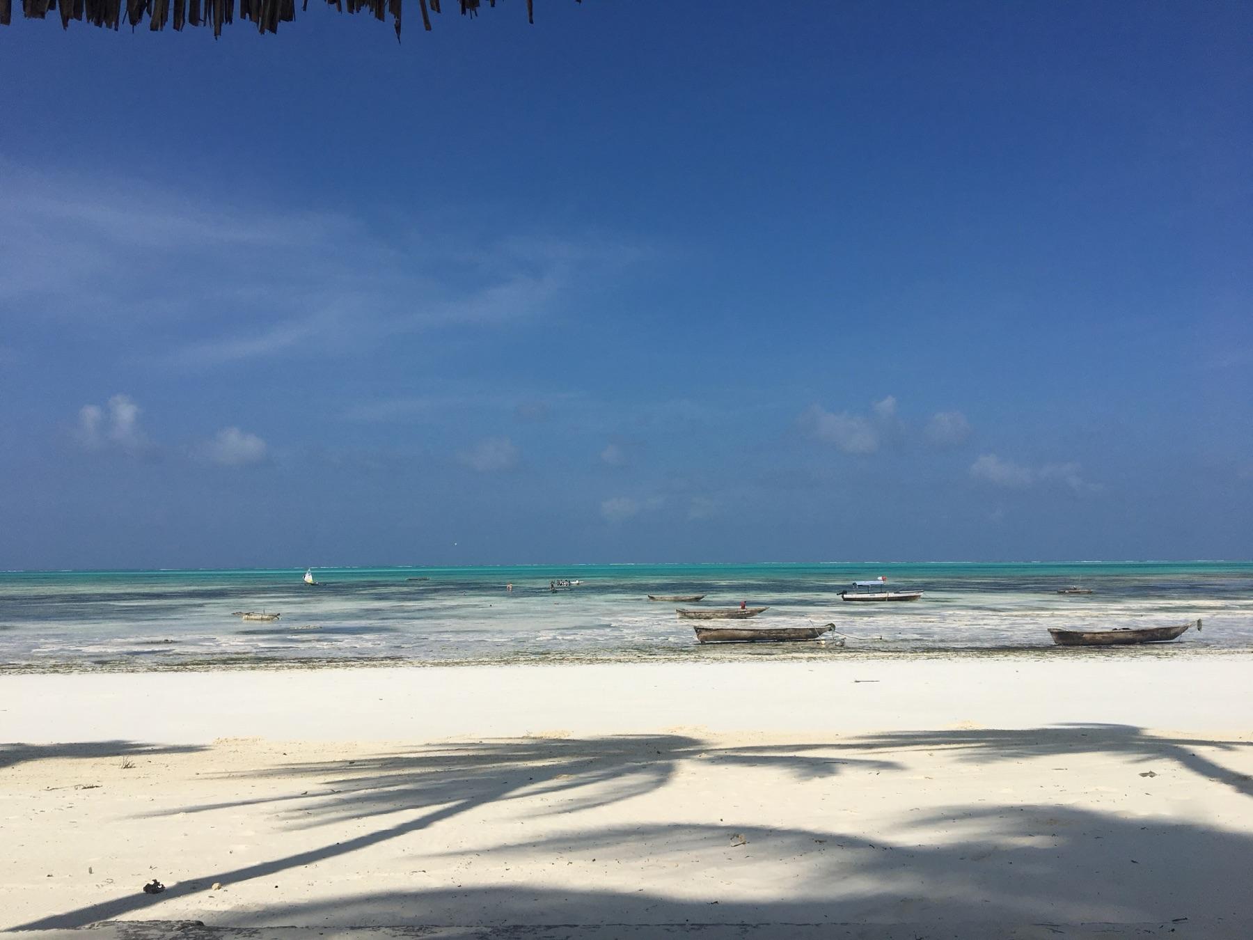 White sand and a turquoise lagoon at low tide in Jambiani, with wooden boats resting in the shallows