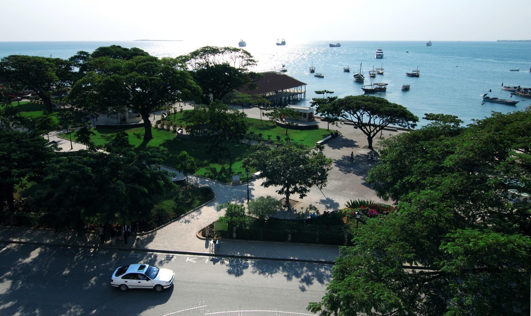 Forodhani Gardens seen from above, shaded by large trees, with boats moored in the harbour beyond