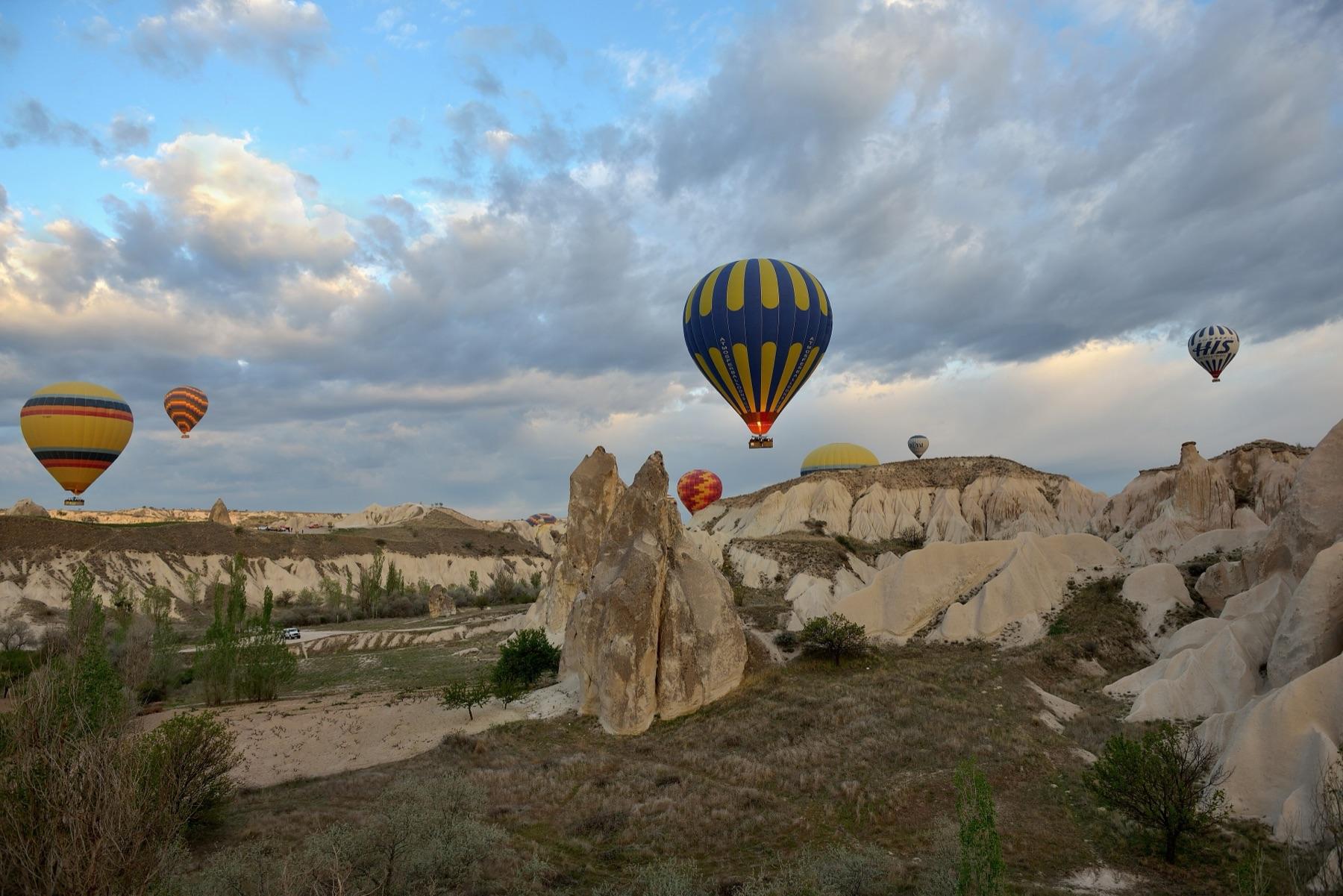 Hot air balloons rise at sunrise over the pale tuff cones and ridges of Cappadocia