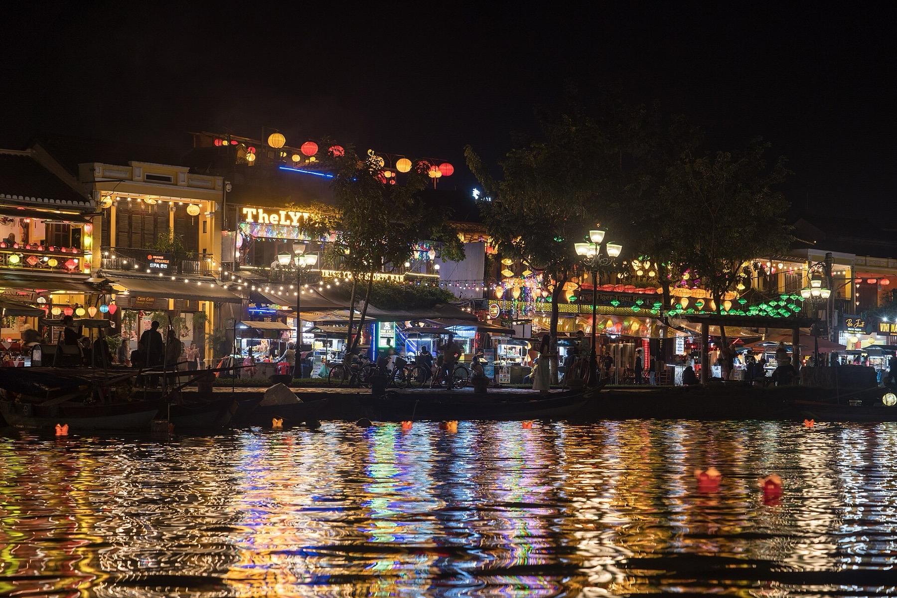 Lanterns and lit shopfronts of Hoi An's old town reflected in the Thu Bon River at night