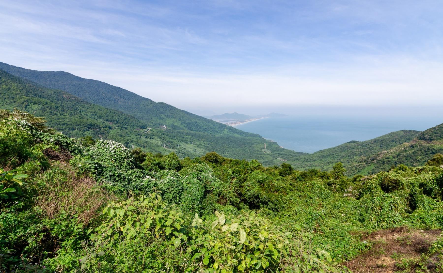 Green forested slopes of the Hai Van Pass running down to the sea, with the sand spit of Lang Co in the distance