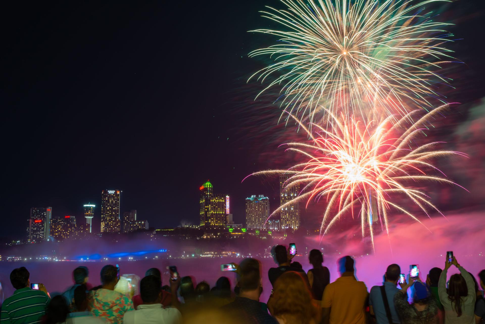 Visitors capturing fireworks over Niagara Falls at night.