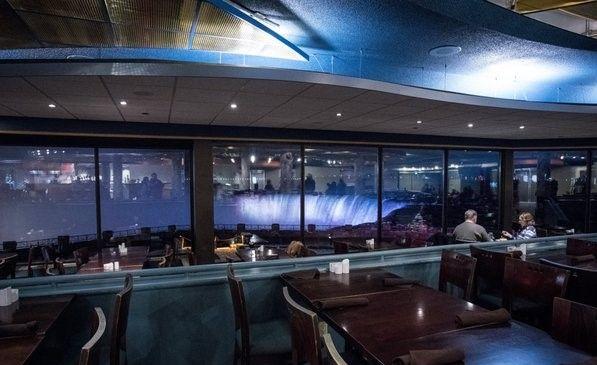 Dining room with large windows overlooking illuminated Niagara Falls at night.