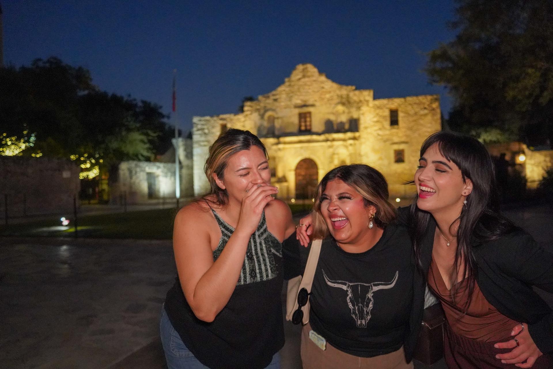 Guests laugh together in front of the Alamo at night